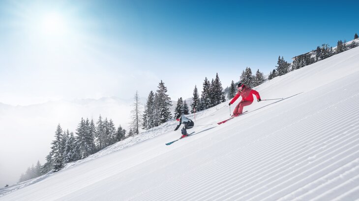 Zwei Skifahrer fahren parallel auf frisch präparierter Skipiste mit Pulverschnee und Sonnenlicht in Ski amadé