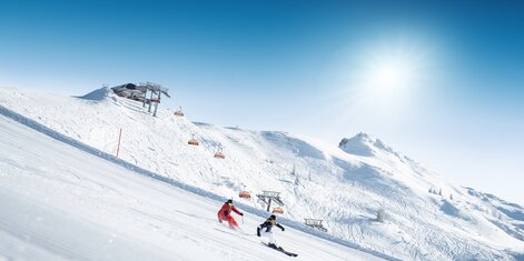 Two skiers carving down a freshly groomed slope on a sunny day | © Ski amadé