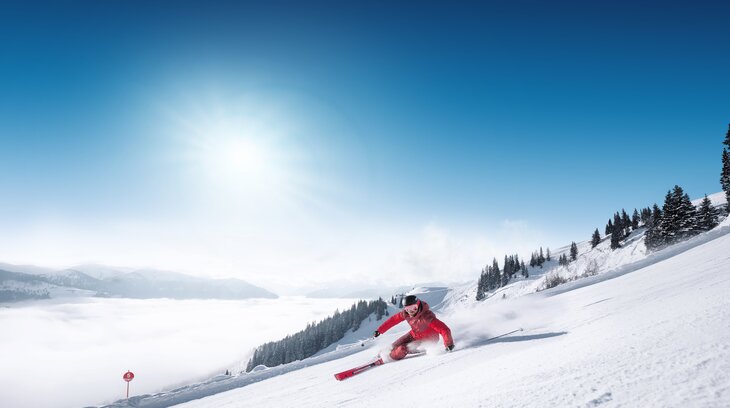 Skier in red suit carves turn on groomed slope with view into the valley in Ski amadé