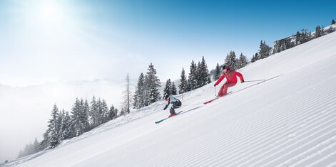 Two skiers ski in parallel on freshly groomed slope with powder snow and sunlight in Ski amadé